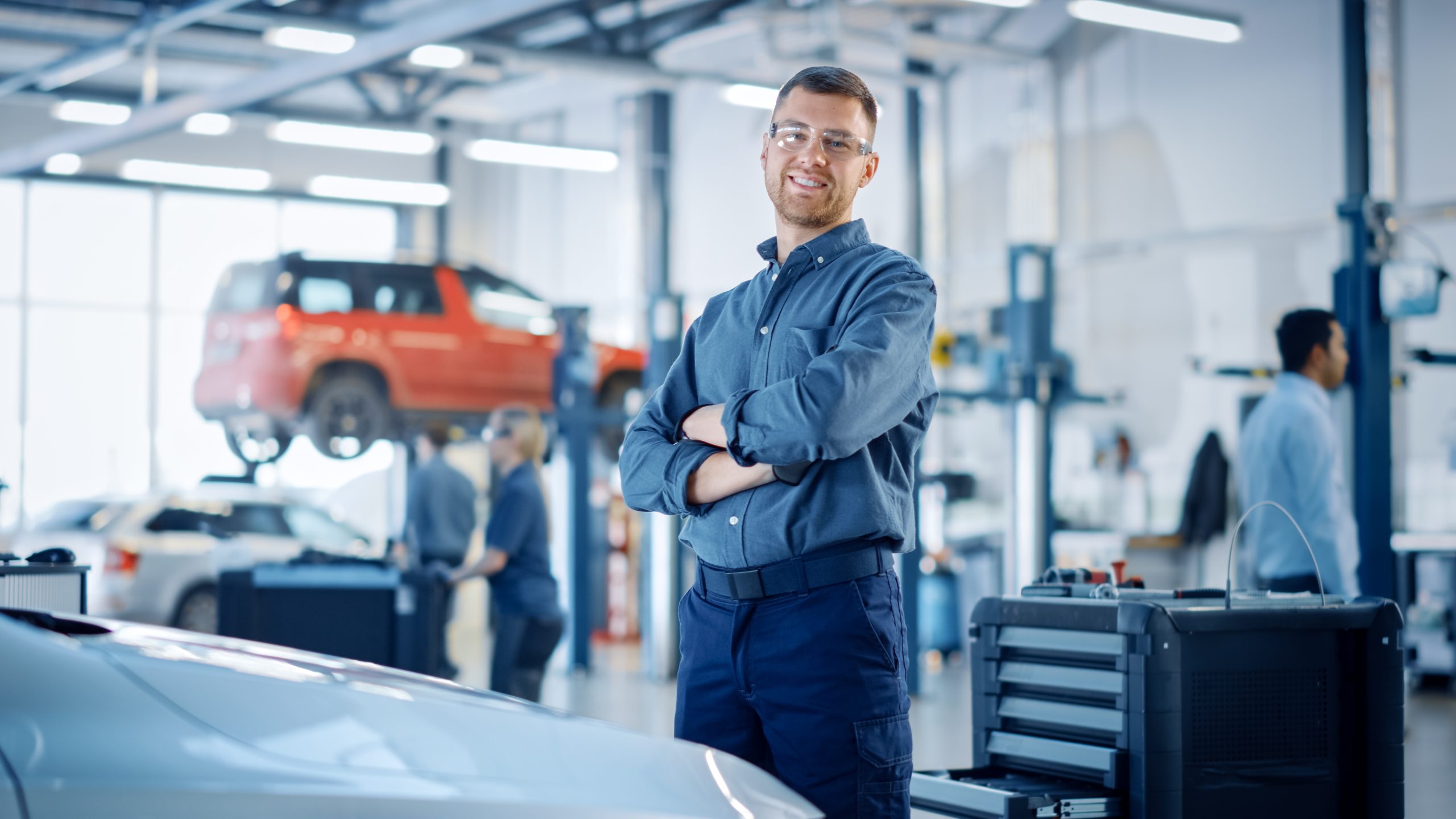 Auto technician standing in a service garage with cars on lifts.